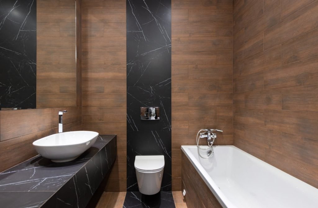 an-interior-of-a-modern-bathroom-7045352 Sleek modern bathroom featuring wood paneling and marble accents, with a white basin and bathtub.
